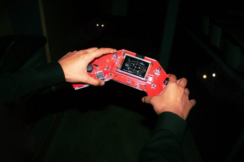 Красное ручное устройство, похожее на Gameboy, с фоном глаз