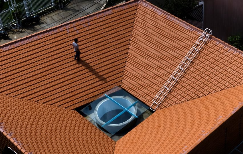 Человек, идущий по красной черепичной крыше дома, построенного The Bloom Architects